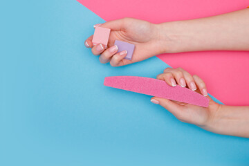 Beautiful female hands with stylish nail manicure gel polish on pink and blue background. Top view. Free space for text. Woman files her nails.