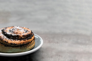 Side view on a tasty bun with poppy seeds lying on a plate on a wooden surface. Copy space