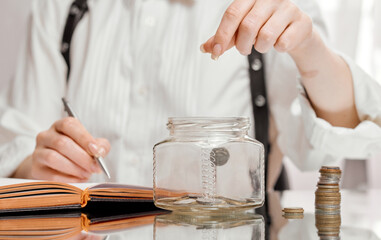 Woman dropping coin into glass jar on mirror table. Savings concept