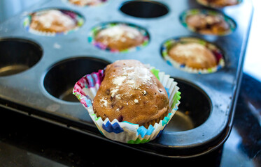 Freshly baked cupcake cakes in two varieties in muffin tin, one standing outside, selected focus, narrow depth of field.