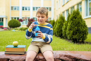 Fototapeta premium Cute schoolboy eating outdoors the school from glass lunch boxe. Food for lunch, lunchboxes with juice, apple and sandwiches, natural fruits.Healthy school breakfast for child.