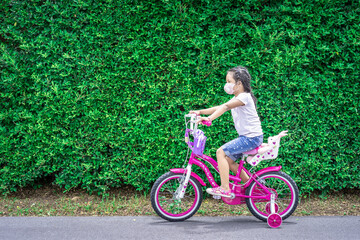 little asian girl wear a mask against PM 2.5 air pollution or coronavirus while ride a bicycle