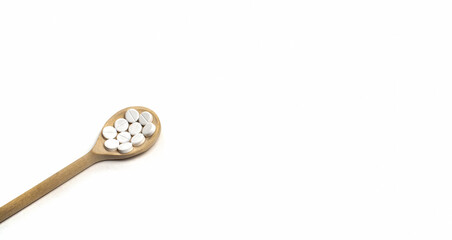 Wooden spoon with round tablets on white background isolated on the left side. Medications on the table for coronavirus, close up. Free space for text. Pills and drugs. Top view. Banner for web site