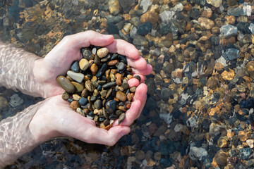 Men's hands hold wet pebbles in the transparent water