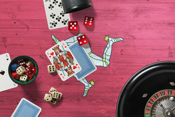 Isle Of Man casino theme. Aces in poker game, cards and chips on red table with national wooden flag background. Gambling and betting.