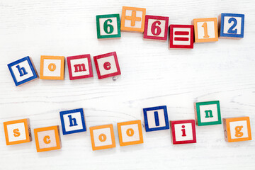 Children’s wooden spelling blocks spell out the words home schooling and a simple sum.