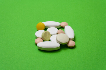Bunch colorful round pills and capsules on a green background close up, macroshot tablets, isolated. Pandemic medications. Drugs disease treatment - covid-19, coronavirus. Vitamins for human health