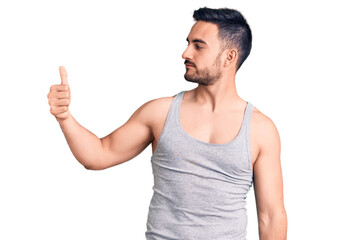 Young handsome man wearing swimwear and sleeveless t-shirt looking proud, smiling doing thumbs up...