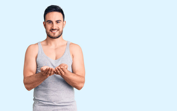 Young handsome man wearing swimwear and sleeveless t-shirt smiling with hands palms together receiving or giving gesture. hold and protection