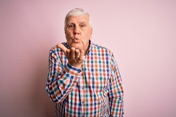 Obraz premium Senior handsome hoary man wearing casual colorful shirt over isolated pink background looking at the camera blowing a kiss with hand on air being lovely and sexy. Love expression.