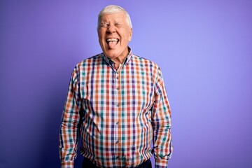 Senior handsome hoary man wearing casual colorful shirt over isolated purple background sticking tongue out happy with funny expression. Emotion concept.