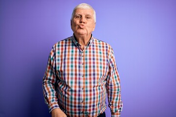Senior handsome hoary man wearing casual colorful shirt over isolated purple background looking at the camera blowing a kiss on air being lovely and sexy. Love expression.