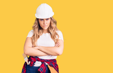 Young caucasian woman wearing security helmet skeptic and nervous, disapproving expression on face with crossed arms. negative person.