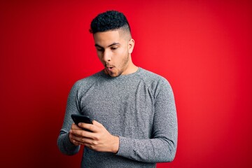 Young handsome man having conversation using smartphone over red background scared in shock with a...