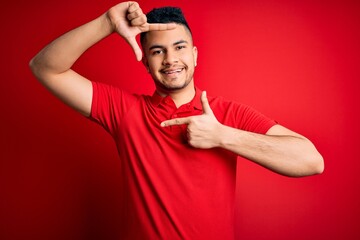 Young handsome man wearing red casual polo standing over isolated background smiling making frame with hands and fingers with happy face. Creativity and photography concept.