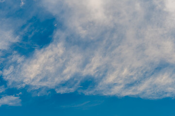Layers of white cirrus clouds in upper atmosphere in blue sky.
