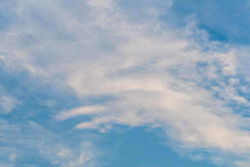 Layers of white cirrus clouds in upper atmosphere in blue sky.