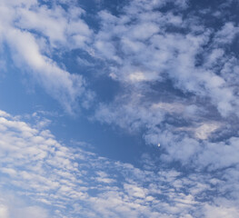 Blue sky with puffy white clouds and a half moon
