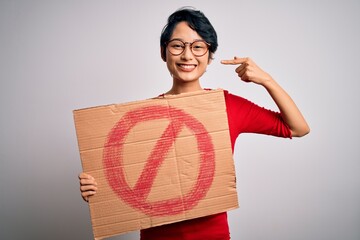 Young beautiful asian girl holding banner with prohibited signal over white background with...