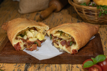 Fogazza stuffed with mozzarella, champignon mushroom, bacon, sun-dried tomatoes and mangering on wooden table with decorated blurred background