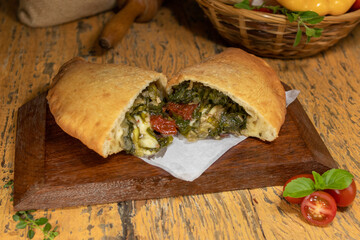 Fogazza stuffed with mozzarella, arugula and sun-dried tomatoes on wooden table with blurred background decorated