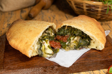 Fogazza stuffed with mozzarella, arugula and sun-dried tomatoes on wooden table with blurred background decorated