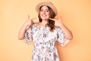 Young beautiful caucasian woman wearing summer dress and hat smiling cheerful showing and pointing with fingers teeth and mouth. dental health concept.