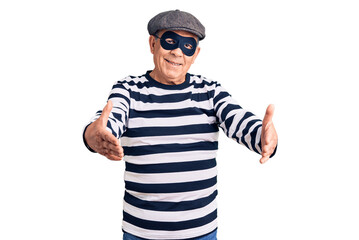 Senior handsome man wearing burglar mask and t-shirt looking at the camera smiling with open arms for hug. cheerful expression embracing happiness.