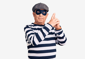 Senior handsome man wearing burglar mask and t-shirt holding symbolic gun with hand gesture, playing killing shooting weapons, angry face