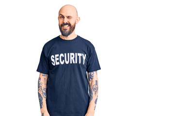Young handsome man wearing security t shirt winking looking at the camera with sexy expression,...