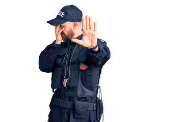 Young handsome man wearing police uniform covering eyes with hands and doing stop gesture with sad and fear expression. embarrassed and negative concept.