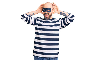 Young handsome man wearing burglar mask smiling cheerful playing peek a boo with hands showing face. surprised and exited