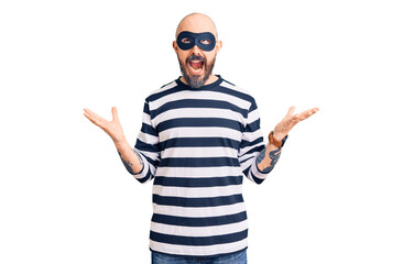 Naklejka premium Young handsome man wearing burglar mask crazy and mad shouting and yelling with aggressive expression and arms raised. frustration concept.