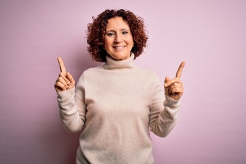 Middle age beautiful curly hair woman wearing casual turtleneck sweater over pink background smiling confident pointing with fingers to different directions. Copy space for advertisement