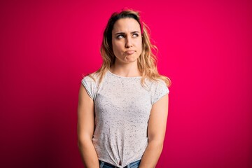 Young beautiful blonde woman wearing casual t-shirt standing over isolated pink background smiling looking to the side and staring away thinking.