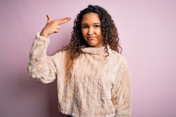 Young beautiful woman with curly hair wearing casual sweater standing over pink background Shooting and killing oneself pointing hand and fingers to head like gun, suicide gesture.