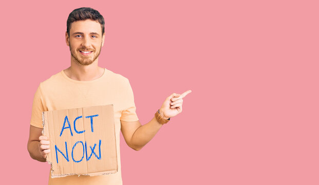 Handsome young man with bear holding act now banner smiling happy pointing with hand and finger to the side