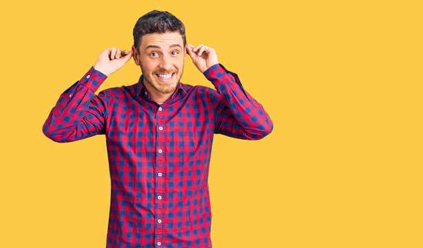 Handsome young man with bear wearing casual shirt smiling pulling ears with fingers, funny gesture. audition problem