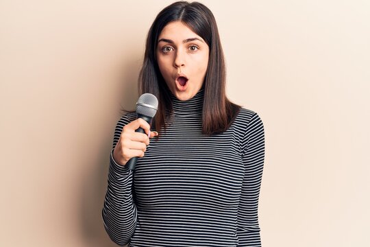 Young beautiful girl singing song using microphone scared and amazed with open mouth for surprise, disbelief face