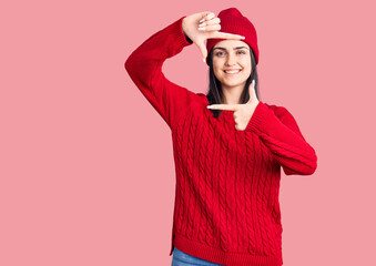 Fototapeta premium Young beautiful girl wearing sweater and wool cap smiling making frame with hands and fingers with happy face. creativity and photography concept.