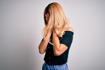Young beautiful blonde woman wearing casual t-shirt standing over isolated white background with sad expression covering face with hands while crying. Depression concept.