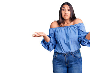 Young beautiful brunette woman wearing casual t-shirt clueless and confused expression with arms...