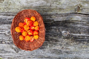 Handful of Cloudberry in wooden basket on an old wooden board background. Healthy diet. Collecting...