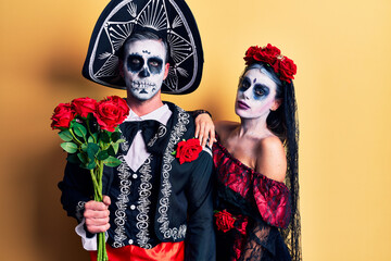 Young couple wearing mexican day of the dead costume holding roses thinking attitude and sober expression looking self confident