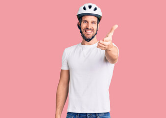 Young handsome man wearing bike helmet smiling friendly offering handshake as greeting and welcoming. successful business.