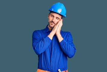 Young handsome man wearing worker uniform and hardhat sleeping tired dreaming and posing with hands together while smiling with closed eyes.