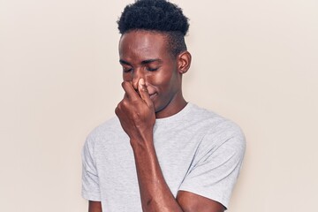 Young african american man wearing casual clothes smelling something stinky and disgusting, intolerable smell, holding breath with fingers on nose. bad smell