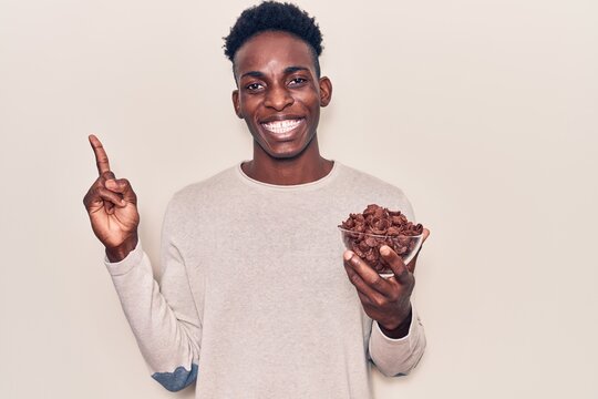 Young african american man holding chocolate cereals smiling happy pointing with hand and finger to the side