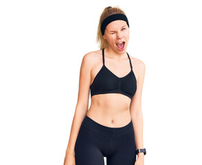 Young beautiful blonde woman wearing sportswear winking looking at the camera with sexy expression,...