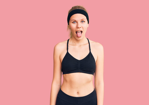 Young beautiful blonde woman wearing sportswear sticking tongue out happy with funny expression. emotion concept.